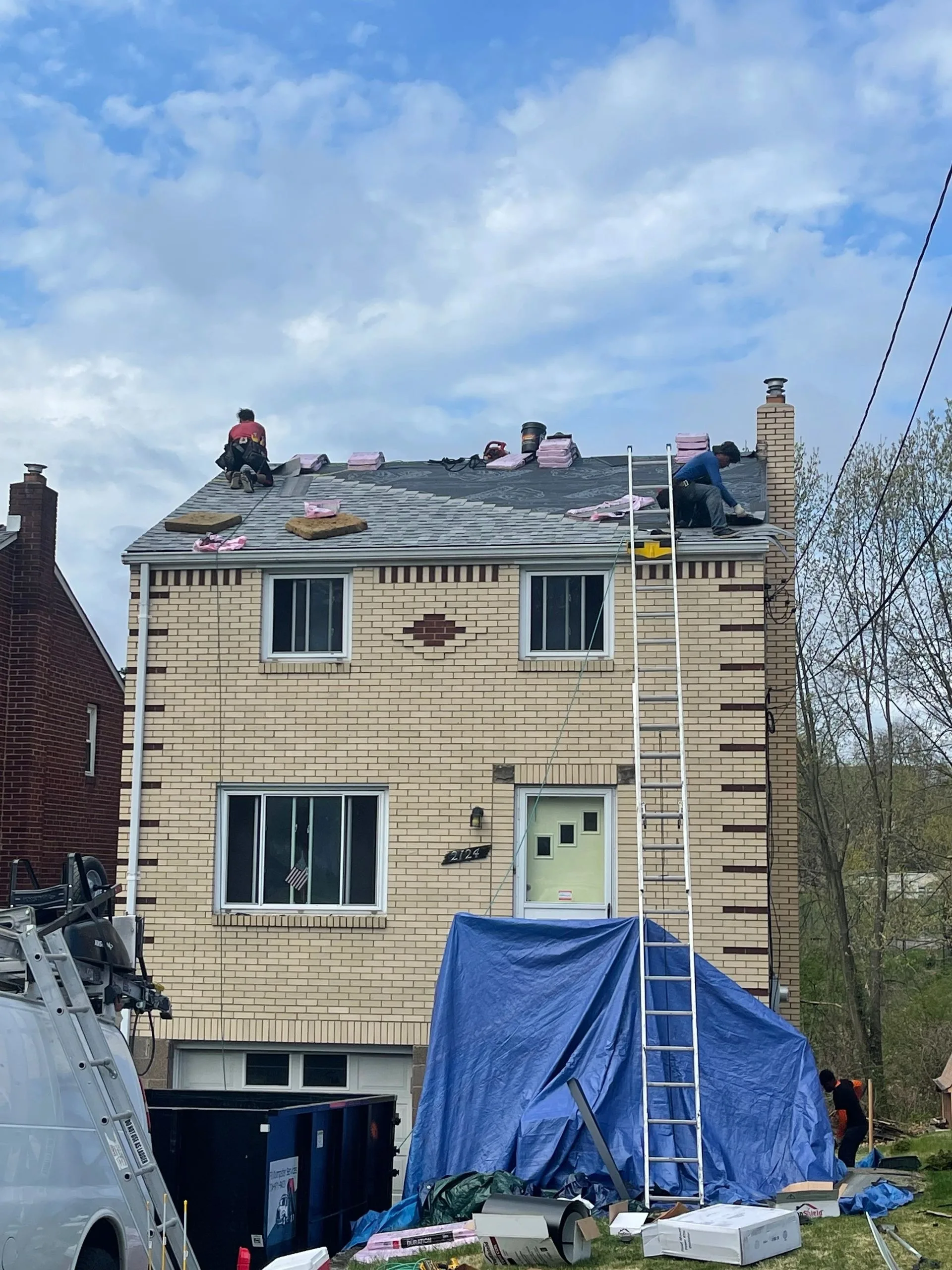 Roofing crew working on a steep residential roof with a tarp protecting the ground below